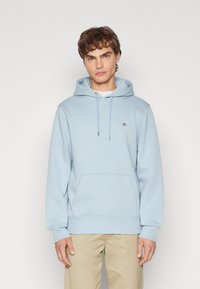 Light blue hoodie made from soft fabric, featuring a front pocket, drawstrings, and a small logo on the left chest.