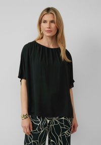 Zwarte, loszittende blouse met een ronde halslijn en korte mouwen, gemaakt van gladde stof. Gecombineerd met gestreepte, lichtgekleurde broek.