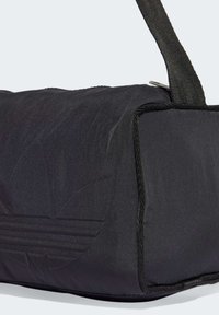Zwarte sporttas met een gladde textuur, featuring een subtiel reliëf logo, en zwarte stiksels en riemdetails. Ritsluiting.