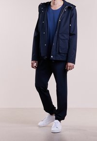 Námořnická modrá nepromokavá bunda s kapucí, na zip, s předními kapsami, v kombinaci s odpovídajícími námořnickými kalhotami a bílými teniskami. Elegantní, minimalistický design.