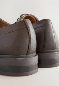 Brown leather shoes with a textured finish, rounded back, and a thick dark sole. Visible stitching detail along the seam.
