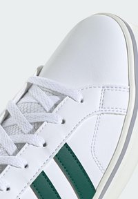 Sneaker bianco sintetico con superficie strutturata, caratterizzato da strisce verdi e lacci bianchi. Punta arrotondata e suola in gomma.