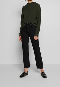 Grön stickad tröja med ribbad textur, svarta raka jeans och svarta loafers. Enkel, modern design utan synliga mönster.