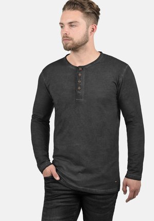 Langærmet sort henley skjorte, lavet af bomuldsmateriale, rund hals, fem brune knapper, subtil tekstur, bøjet søm, parret med mørke jeans.
