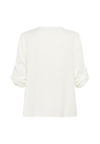 Top bianco e strutturato con maniche lunghe. Le maniche sono arrotolate e fissate con delle linguette. Design semplice e morbido con scollo a girocollo.