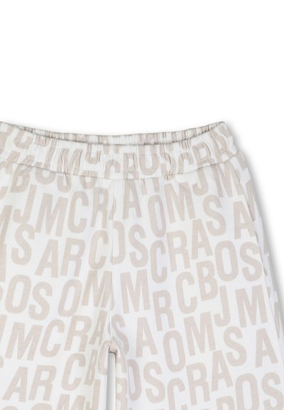Close-up van witte broek met elastische tailleband en beige verspreide hoofdletters die een willekeurig patroon vormen op de stof.