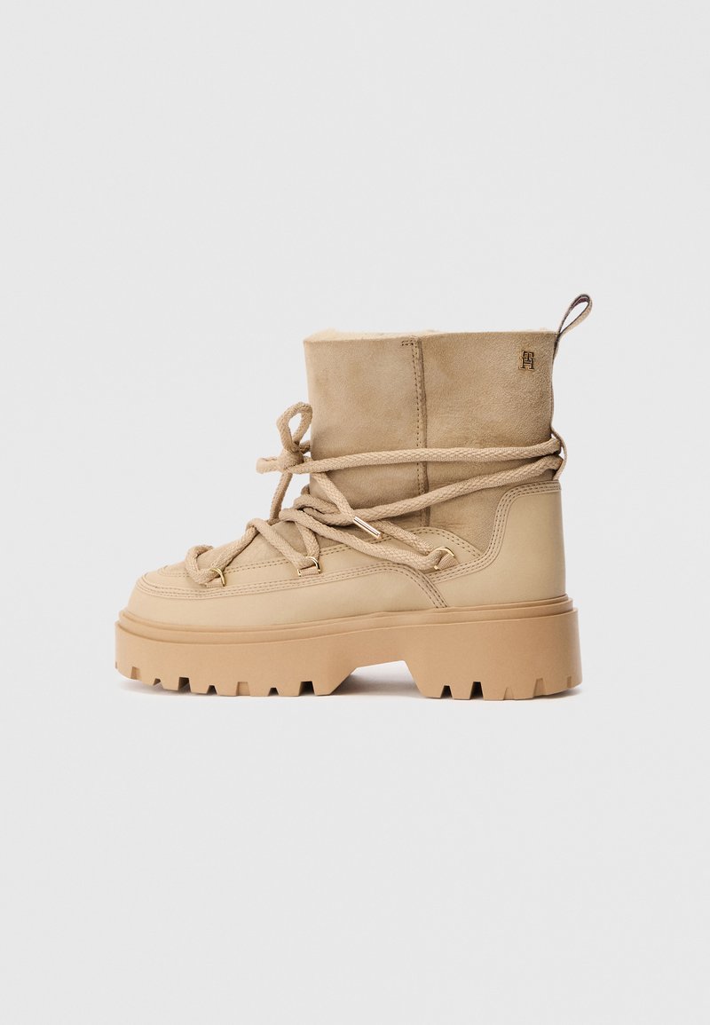 Beżowe botki za kostkę z zamszową cholewką, grubą gumową podeszwą i teksturowanymi sznurówkami. Posiadają małe logo po boku oraz pętelkę przy pięcie.