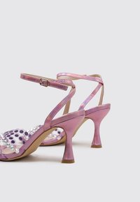Sandalias de tacón rosas con un acabado brillante, con un diseño de lunares y cuentas decorativas. Tiras de conexión con hebillas.