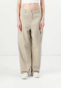 Beige cargobyxor i bomull med avslappnad passform, två sidofickor och knäppning vid midjan. Kombinationen med vita sneakers.