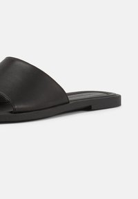 Μαύρο δερμάτινο σανδάλι σλάιντ με φαρδιά μονή λουρίδα και επίπεδη σόλα, εμφανιζόμενο σε λευκό φόντο, σε πλάγια γωνία.