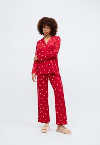 Κόκκινο πιτζάμα σετ με λευκά σχέδια καρδιάς. Μακρυμάνικο πουκάμισο με κουμπιά, σε συνδυασμό με αντίστοιχες παντελόνες. Μαλακό ύφασμα με σχέδιο ίσιας κνήμης.