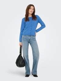 Cardigan en tricot bleu à manches longues avec fermeture à boutons, associé à un jean bleu clair à jambes larges et un sac hobo noir.