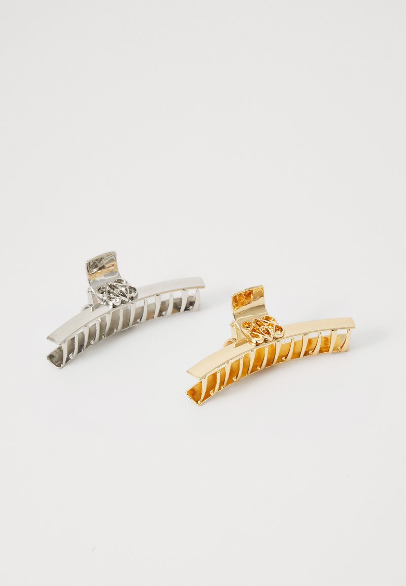 Két hajcsat: az egyik ezüst, a másik arany. Mindkettő ívelt formájú, kivágott mintákkal és texturált markolattal rendelkezik a haj biztonságos tartásához.