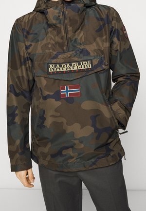 Napapijri jakke med camouflage mønster, hætte, frontlomme, norsk flagpatch og lynlåslommer i siden båret af en person.