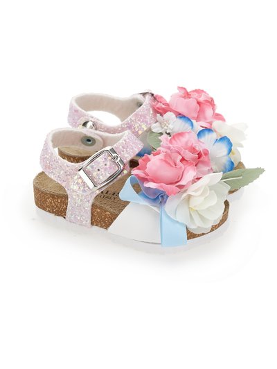 Παιδικά σανδάλια με φελλό στις σόλες, ιριδίζοντες ροζ ιμάντες, ασημένιες αγκράφες και διακοσμητικά υφασμάτινα λουλούδια σε ροζ, λευκό και μπλε χρώμα στην κορυφή.