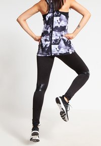 Leggings sportivi neri con un'accento lucido nera sulle ginocchia, abbinati a una maglietta senza maniche con motivo geometrico in nero e grigio.