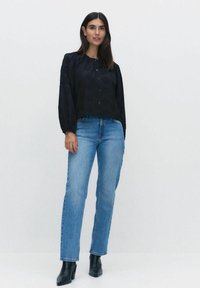 Svart, texturerad blus med rund halsringning och knappstängning, kombinerad med ljusblå raka jeans och svarta ankelboots.