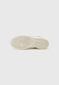 Hvid sneakersål med mønstret slidbane, der har et cirkulært design i midten og tynde riller til greb, lavet af gummimateriale.