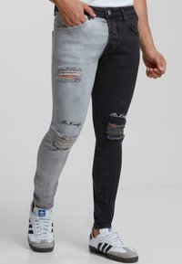 Jeans ajustados con un diseño bicolor, una pierna en gris claro y la otra en negro, desgastados con rotos y acentos bordados.