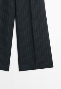 Donkergrijze wijde broek met krijtstreep en een gespleten zoomdetail aan de onderkant tegen een witte achtergrond.