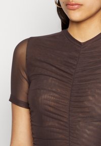 Top castanho de manga curta feito de tecido leve e transparente, com textura franzida e decote em V.