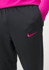 Schwarze Sporthosen mit glatter Textur, die auf der Seite ein pinkes Nike-Logo und einen leicht elastischen Bund aufweisen.