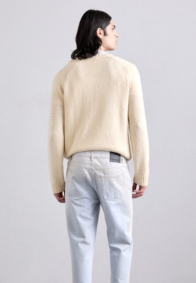 Cream knit sweater with a textured finish, paired with light blue denim jeans featuring a regular fit and visible back pockets.