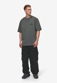 Overdimensioneret grå t-shirt med korte ærmer og et lille logo, parret med sorte cargo-bukser med flere lommer og mørke sneakers.