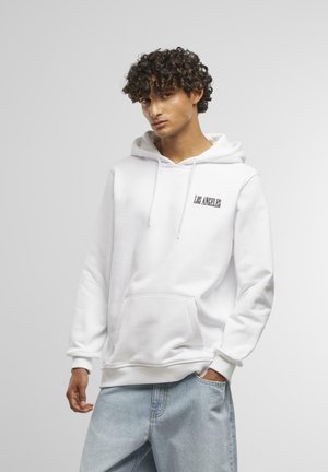 Weißer Sweatpullover mit "LOS ANGELES" Schriftzug, frontaler Tasche und Kapuze mit Kordelzug, kombiniert mit hellblauen Jeans. Sanfte Textur und lässige Passform.