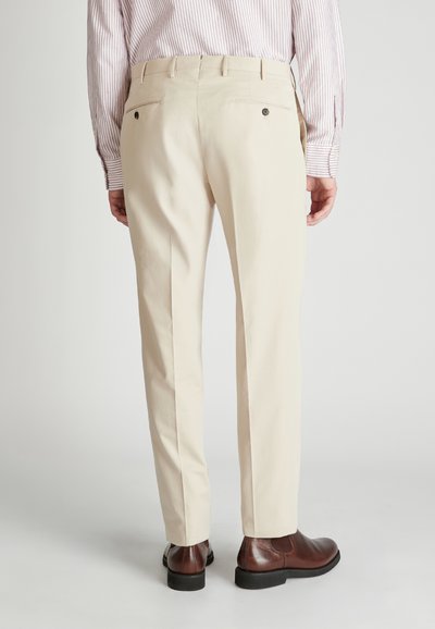 Beige maßgeschneiderte Hose aus Baumwolle mit glatter Textur, ausgestattet mit zwei Gesäßtaschen und dezenten Nahtdetails. Braune Lederschuhe sind enthalten.