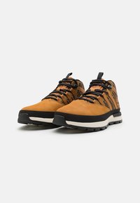 Braune Wildleder-Wanderschuhe mit schwarzen Akzenten, ausgestattet mit strapazierfähigen Schnürsenkeln, einer strukturierten Oberfläche und einer dicken weißen Zwischensohle für Unterstützung.