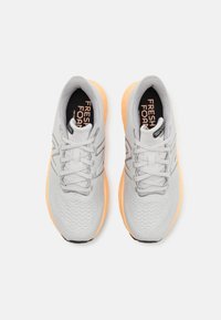 Jasnoszare buty sportowe z fakturowaną cholewką, pomarańczową podeszwą i odblaskowymi detalami. Posiadają płaskie sznurówki oraz oznaczenie "Fresh Foam" wewnątrz.