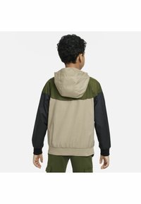 Chaqueta con capucha de cuerpo beige, hombros verdes y mangas negras. Presenta puños elásticos y un tejido suave y ligero.