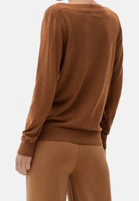 Brauner Strickpullover mit langen Ärmeln, einem gerippten Kragen und Saum. Weicher Stoff, lockere Passform, kombiniert mit passenden braunen Hosen.