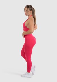 Roze sportcrop top en leggings gemaakt van rekbaar materiaal, gecombineerd met witte sportschoenen. Het design heeft een eenvoudige uitstraling en een hoge taille.