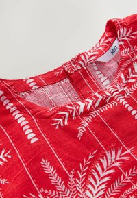 Rotes Stoffoberteil mit floralem weißen Druck, rundem Ausschnitt und einem kleinen Schlüssellochdetail auf der Rückseite. Weiches, strukturiertes Material.