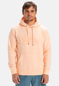 Peach-colored sweatshirt with a hood, large front pocket, and subtle logo detail. Soft texture and adjustable drawstrings.