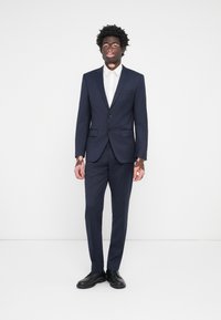 Costum bleumarin cu un design ajustat, două butoane, rever în clopot, asortat cu o cămașă albă și pantofi negri de ocazie. Țesătură netedă, ajustare pe măsură.