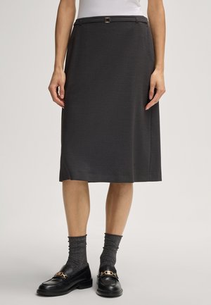 Donkergrijze jurk tot de knie van een gestructureerde stof, met een slanke riem en een subtiele glans, gecombineerd met zwarte loafers en grijze sokken.