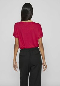Top rosso a maniche corte e taglio morbido, realizzato in tessuto leggero, abbinato a pantaloni neri a vita alta con tasche laterali e vita elasticizzata.
