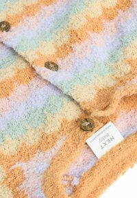 Couverture pour bébé en tricot dans des couleurs pastel (orange, vert, jaune, lavande) avec un motif texturé et duveteux et deux boutons décoratifs.