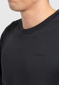 Zwarte katoenen sweatshirt met een ronde hals en een textuurstof, met een subtiele logo op de borst. Close-upweergave.