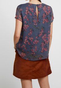 Floral blouse in dark blue fabric with pink and green flowers; features short sleeves, a keyhole back, and a slightly curved hem.