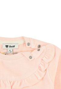 Camiseta infantil de color rosa claro con cuello con volantes, cierres a presión y una etiqueta de tela con un logo de oso. Textura suave, adecuada para edades de 2 a 3 meses.