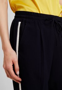 Marina atletiska byxor med elastisk midja, dragsko och vita sidostråk. Slät tyg med fickor och avslappnad passform.