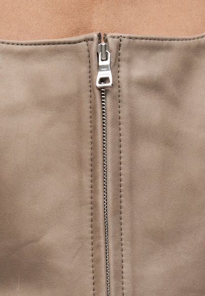 Κοντινή λήψη ενός μπεζ δερμάτινου ενδύματος με ασημένιο μεταλλικό φερμουάρ στο κέντρο, μερικώς κλειστό.