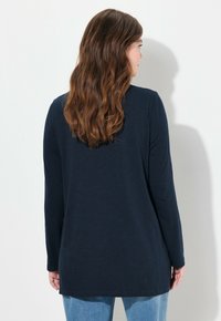 Marineblaues Langarmoberteil mit lockerer Passform, geradem Schnitt und Rundhalsausschnitt, aus weichem Jersey-Stoff, kombiniert mit hellblauen Jeans.