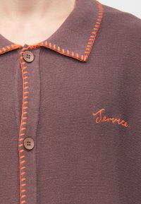 Polokošeľa s krátkym rukávom tmavofialovej farby s oranžovým prešitím na golieri a zapínaní na gombíky, s vyšívaným nápisom „Service“ v oranžovej farbe.