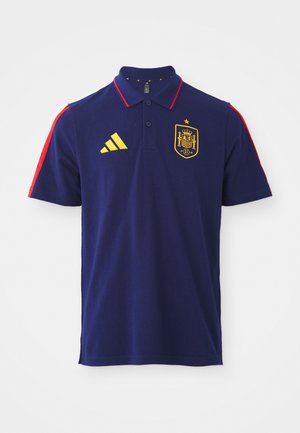 Mornarsko plava polo majica s crvenim detaljima, žutim Adidas logotipom i španjolskim nacionalnim emblemom. Izrađena od pamuka, ima klasični ovratnik i kopčanje na gumbe.