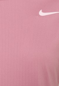 Růžový top s krátkým rukávem vyrobený z texturované pleteniny, s jemným vertikálním žebrovaným vzorem a malým bílým logem Nike swoosh.